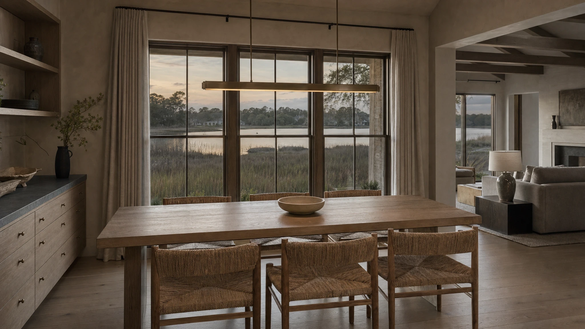 Lynnhaven House dining room with a white-oak table, woven-rush chairs, and tidal-creek windows at low evening light
